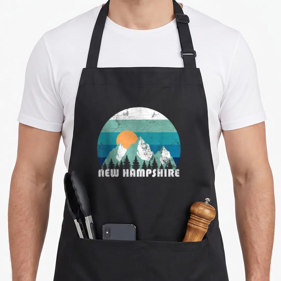 State hampshire girl apron - Retro New Hampshire mountain landscape with orange sun, striped sky, and trees — shown on a black cotton canvas apron against a white background