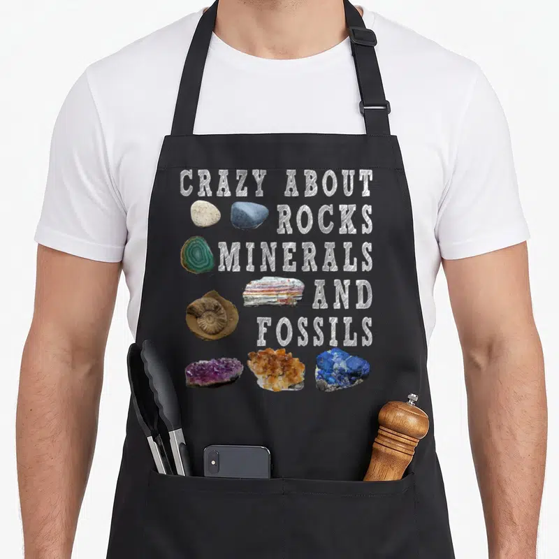 Mineral teacher apron - Stacked white text next to purple, blue, orange, and grey rock specimens on black background — shown on a black cotton canvas apron against a white background