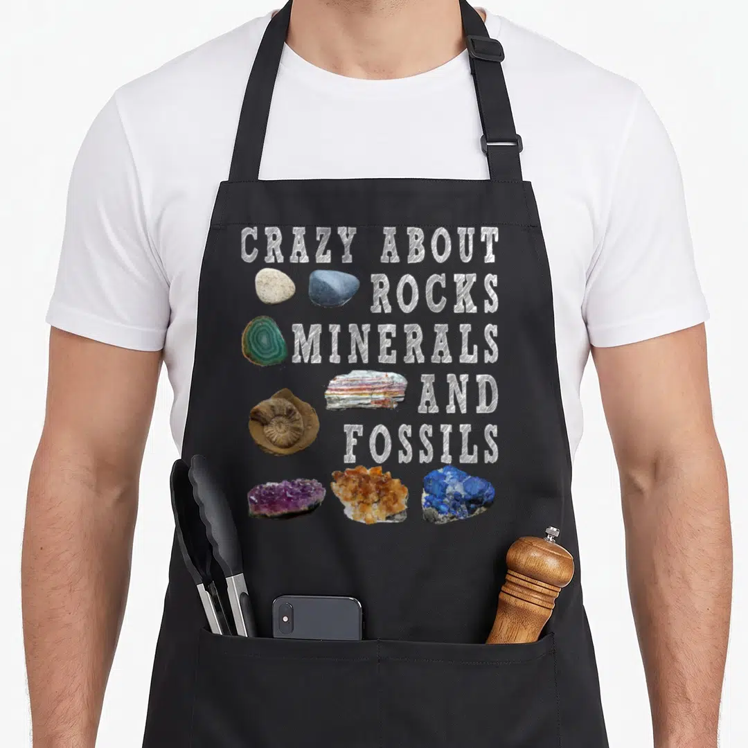 Mineral teacher apron - Stacked white text next to purple, blue, orange, and grey rock specimens on black background — shown on a black cotton canvas apron against a white background