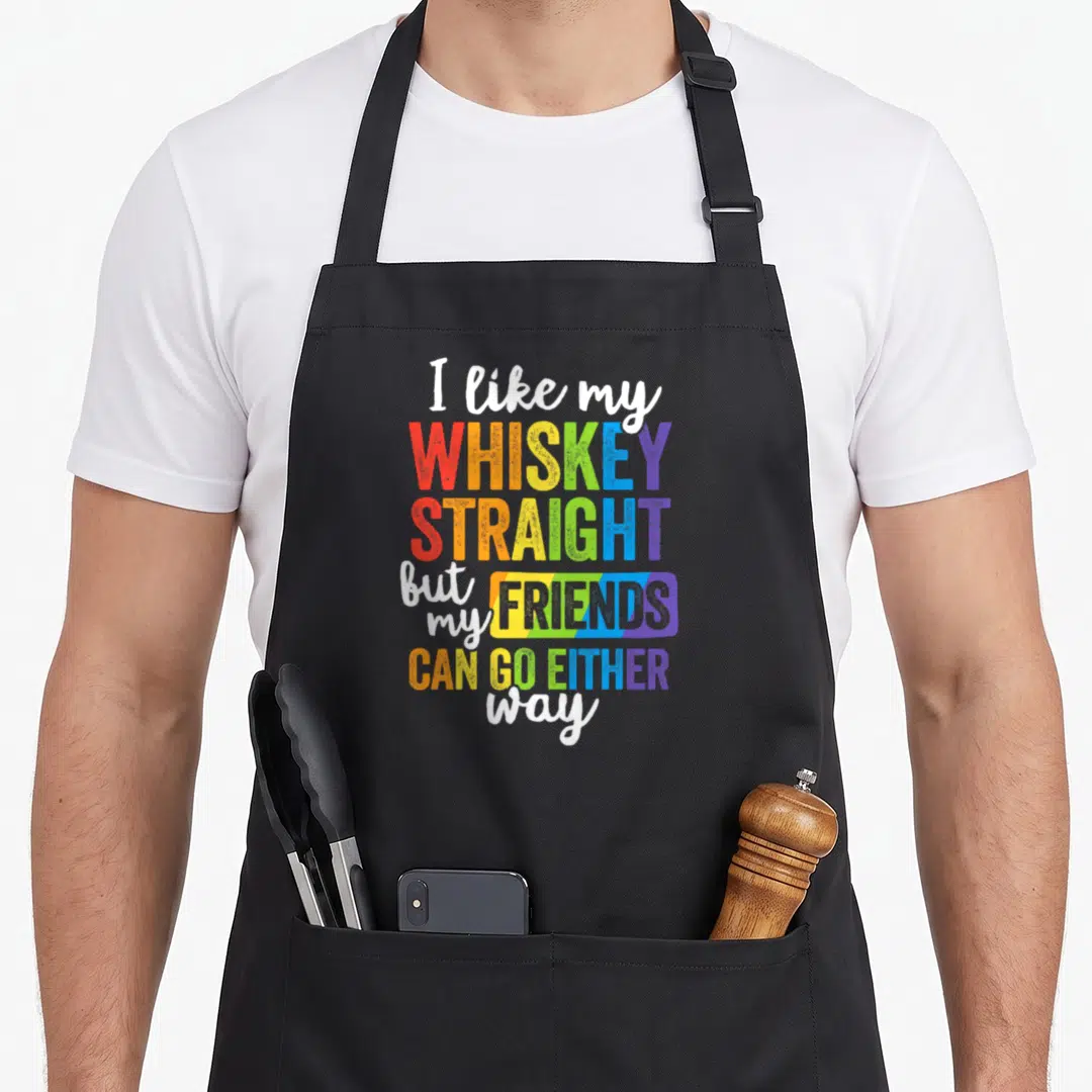 Whiskey gay pride apron - Rainbow text reading I like my WHISKEY STRAIGHT but my FRIENDS CAN GO EITHER way on black — shown on a black cotton canvas apron against a white background