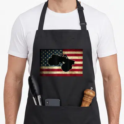 Car truck aprons - Black monster truck silhouette on distressed red white and blue flag pattern — shown on a black cotton canvas apron against a white background