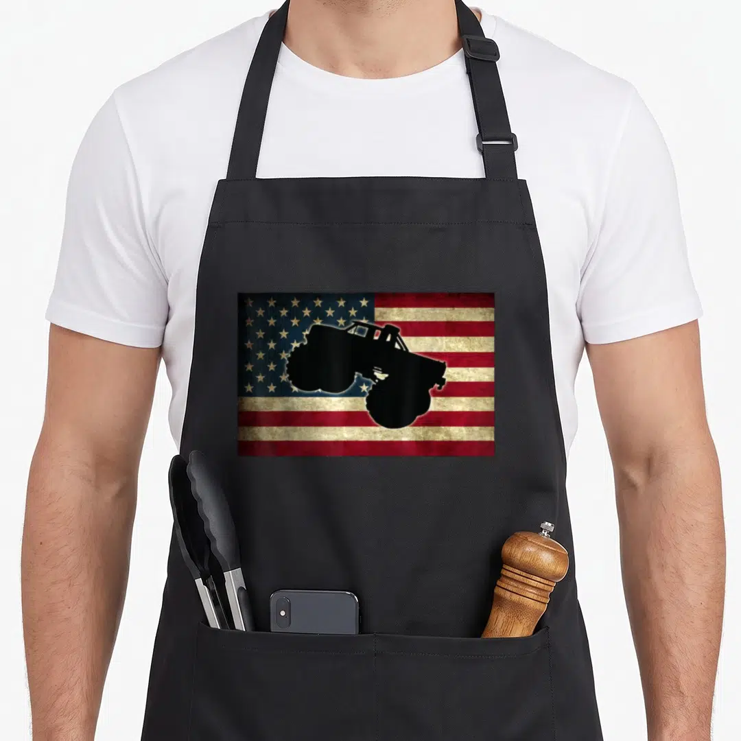 Car truck aprons - Black monster truck silhouette on distressed red white and blue flag pattern — shown on a black cotton canvas apron against a white background