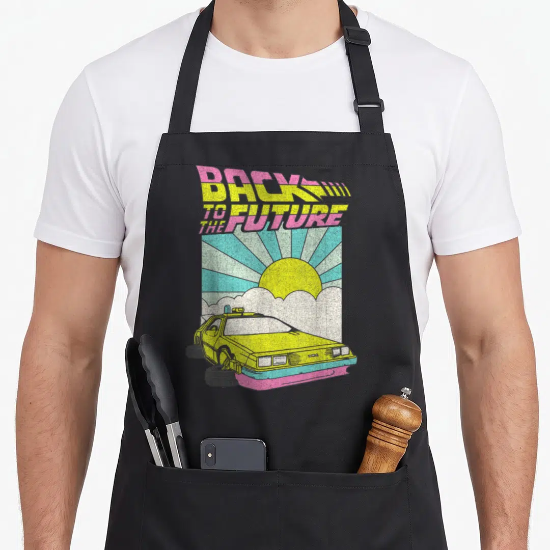 Delorean cartoon apron - Back to the Future text above yellow car with pink blue sun rays — shown on a black cotton canvas apron against a white background