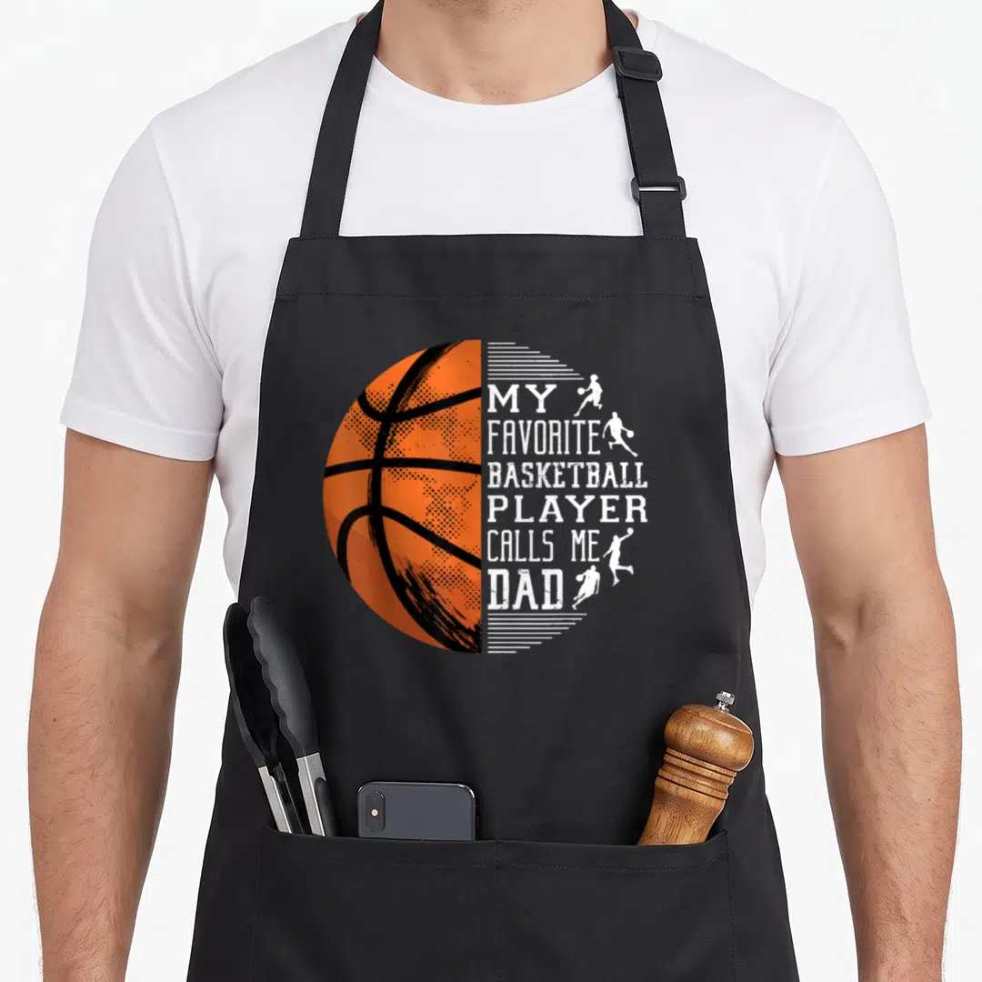 Basketball proud dad apron - Orange half basketball next to stacked white text reading My Favorite Basketball Player — shown on a black cotton canvas apron against a white background
