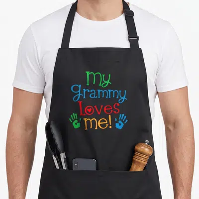 Grandson grammy apron - My Grammy Loves me! text with heart and two handprints in green, blue, red, orange — shown on a black cotton canvas apron against a white background
