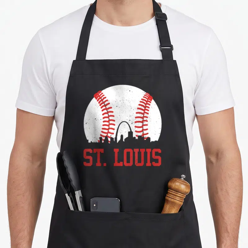 Cityscape baseball apron - White baseball with red stitching overlapping St. Louis skyline and ST. LOUIS text — shown on a black cotton canvas apron against a white background