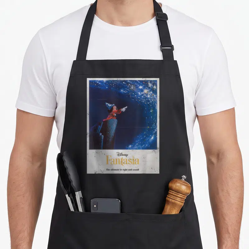 Fantasia mouse lover apron - Mickey Mouse in red robe pointing at stars above yellow Fantasia text and slogan on blue — shown on a black cotton canvas apron against a white background