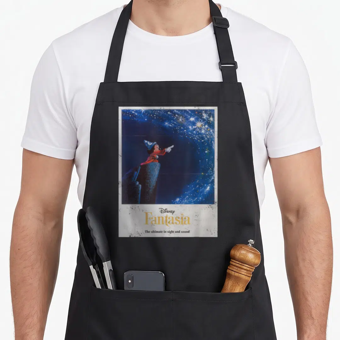 Fantasia mouse lover apron - Mickey Mouse in red robe pointing at stars above yellow Fantasia text and slogan on blue — shown on a black cotton canvas apron against a white background