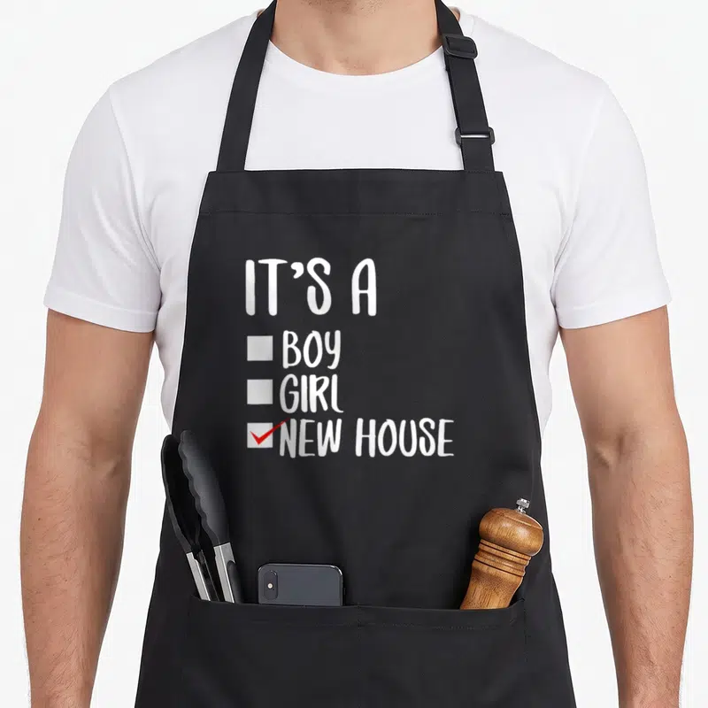Cool occasion novelty apron - White checklist text IT'S A BOY GIRL NEW HOUSE with red checkmark — shown on a black cotton canvas apron against a white background