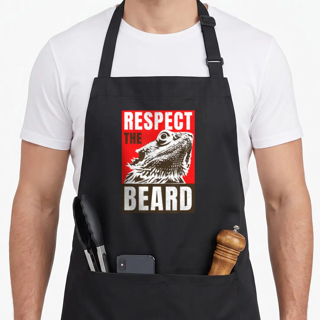 Respect daddy apron - Distressed red and brown graphic of a bearded dragon head with Respect The Beard text — shown on a black cotton canvas apron against a white background