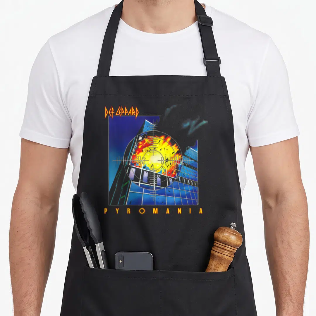 Def crew apron - Def Leppard Pyromania exploding building through crosshairs in blue orange yellow red — shown on a black cotton canvas apron against a white background