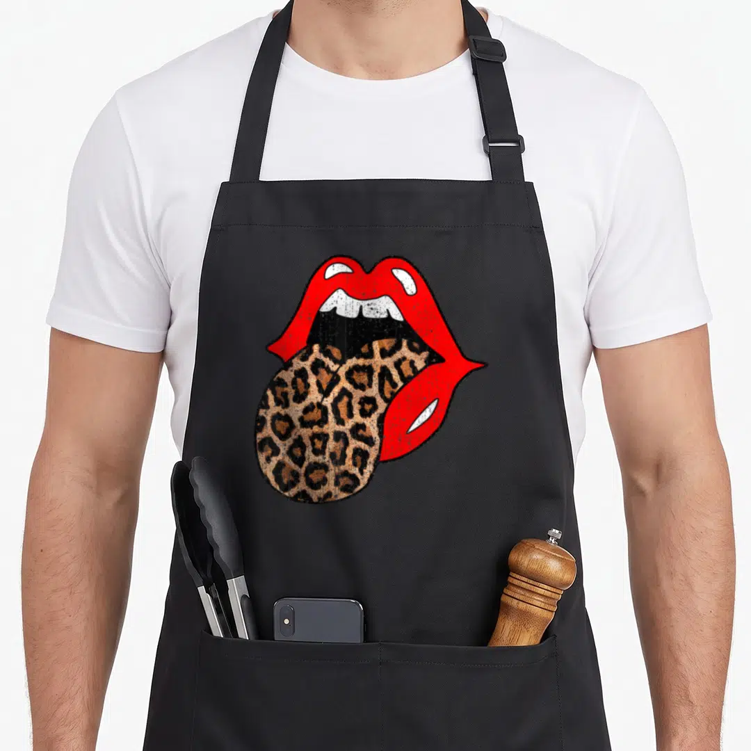Lip leopard print apron - Red lips and white teeth with a leopard print tongue hanging down to the left — shown on a black cotton canvas apron against a white background