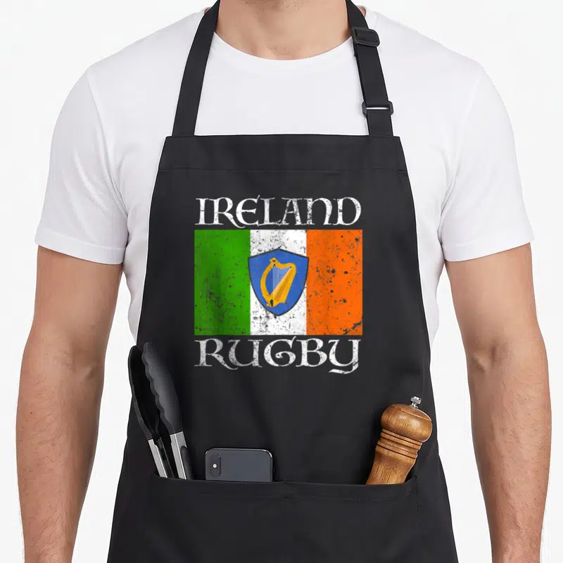 Fan ireland apron - Distressed Irish flag with blue shield gold harp and text IRELAND RUGBY — shown on a black cotton canvas apron against a white background