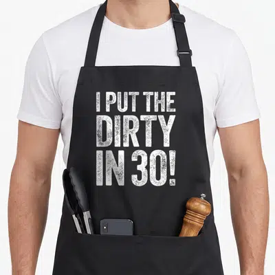Thirty the dirty apron - White stacked text I PUT THE DIRTY IN 30 on black background — shown on a black cotton canvas apron against a white background