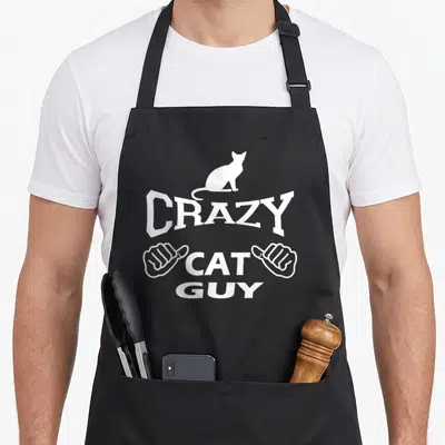 Pet black cat aprons - White line art of a cat sitting on the word crazy flanked by two thumbs up hands — shown on a black cotton canvas apron against a white background