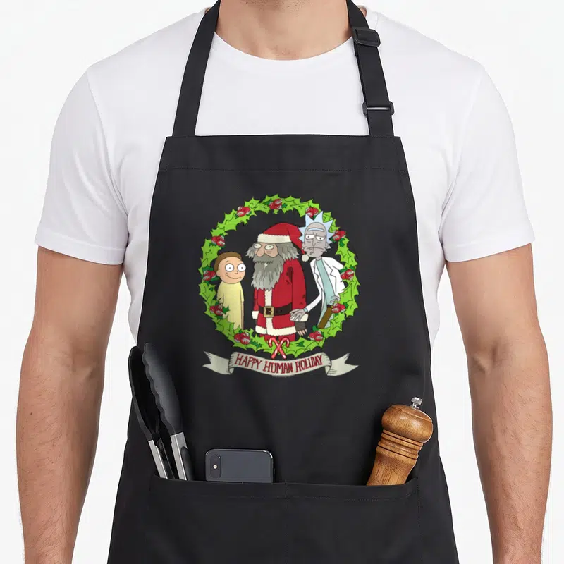 Human holiday apron - Three cartoon figures in green wreath with red accents and HAPPY HUMAN HOLIDAY text on ribbon — shown on a black cotton canvas apron against a white background