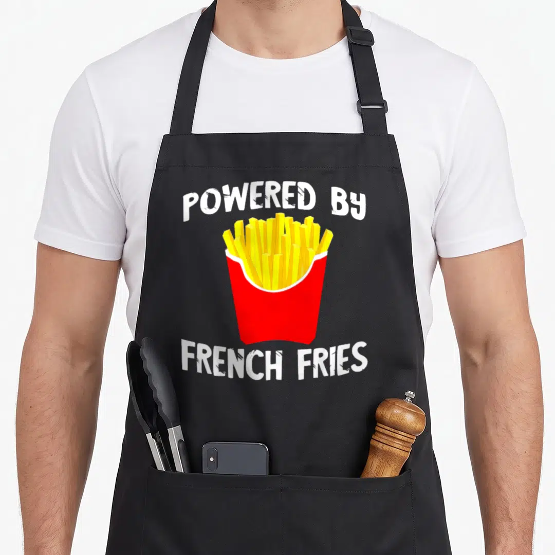 Powered french apron - Cartoon red carton of yellow french fries with white arched text POWERED BY FRENCH FRIES — shown on a black cotton canvas apron against a white background