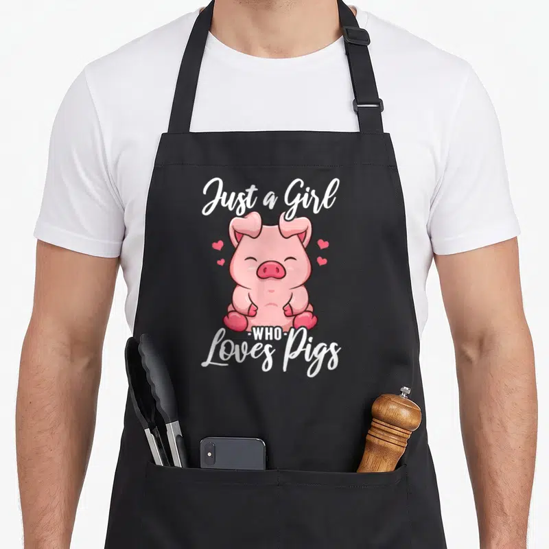 Funny pig lover apron - Pink cartoon pig surrounded by hearts with white text Just a Girl Who Loves Pigs — shown on a black cotton canvas apron against a white background