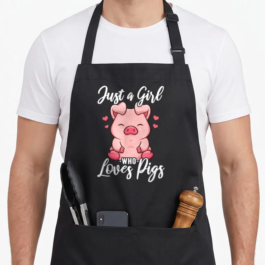 Funny pig lover apron - Pink cartoon pig surrounded by hearts with white text Just a Girl Who Loves Pigs — shown on a black cotton canvas apron against a white background