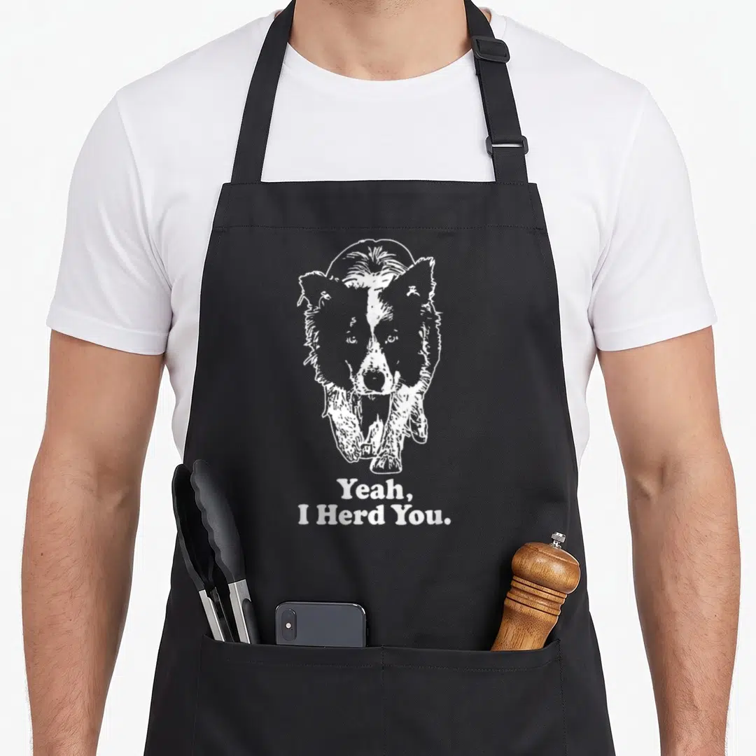 Yeah border collie apron - White line-art dog portrait above stacked text Yeah I Herd You — shown on a black cotton canvas apron against a white background