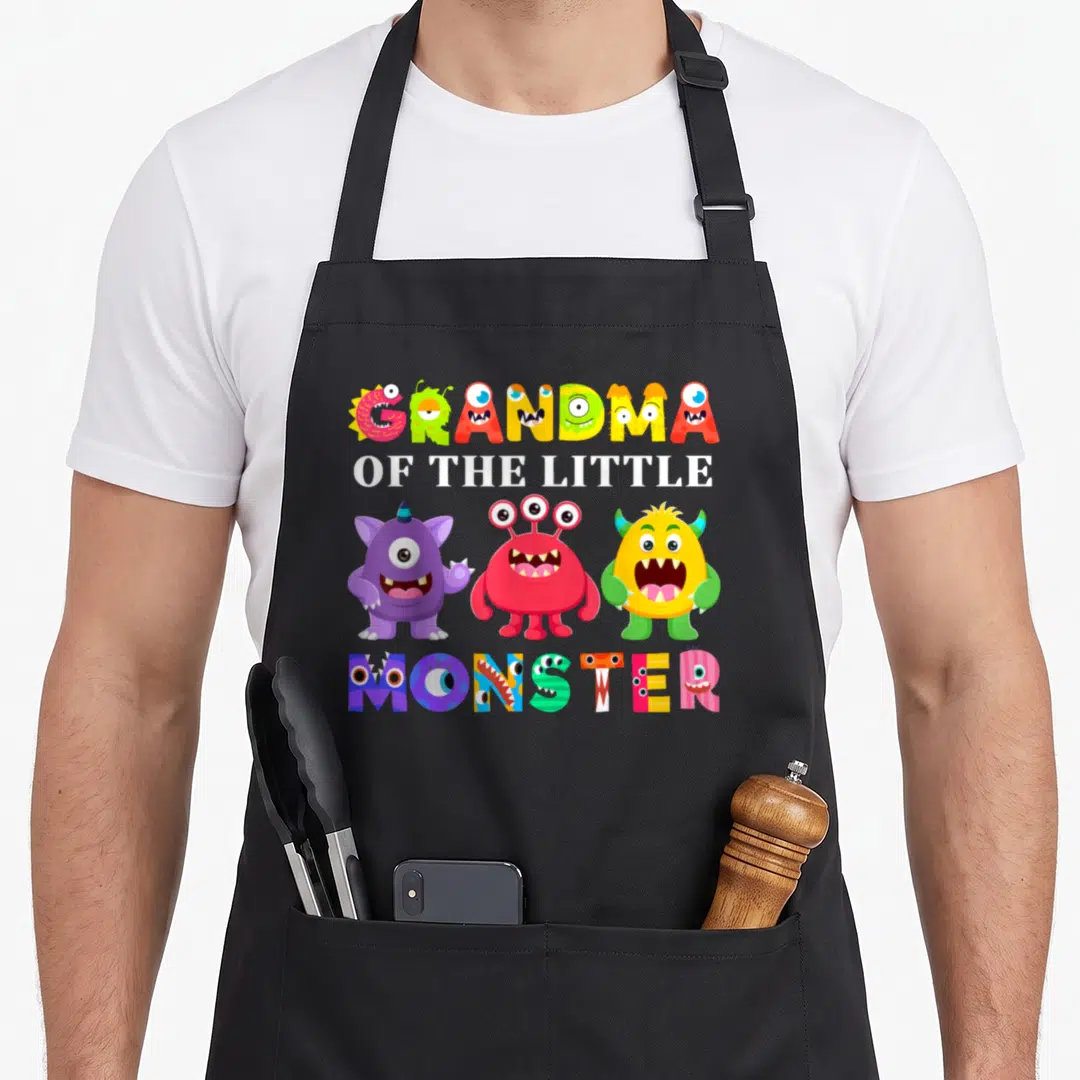 Monster grandma in apron - Three colorful cartoon monsters below GRANDMA OF THE LITTLE MONSTER text in white — shown on a black cotton canvas apron against a white background