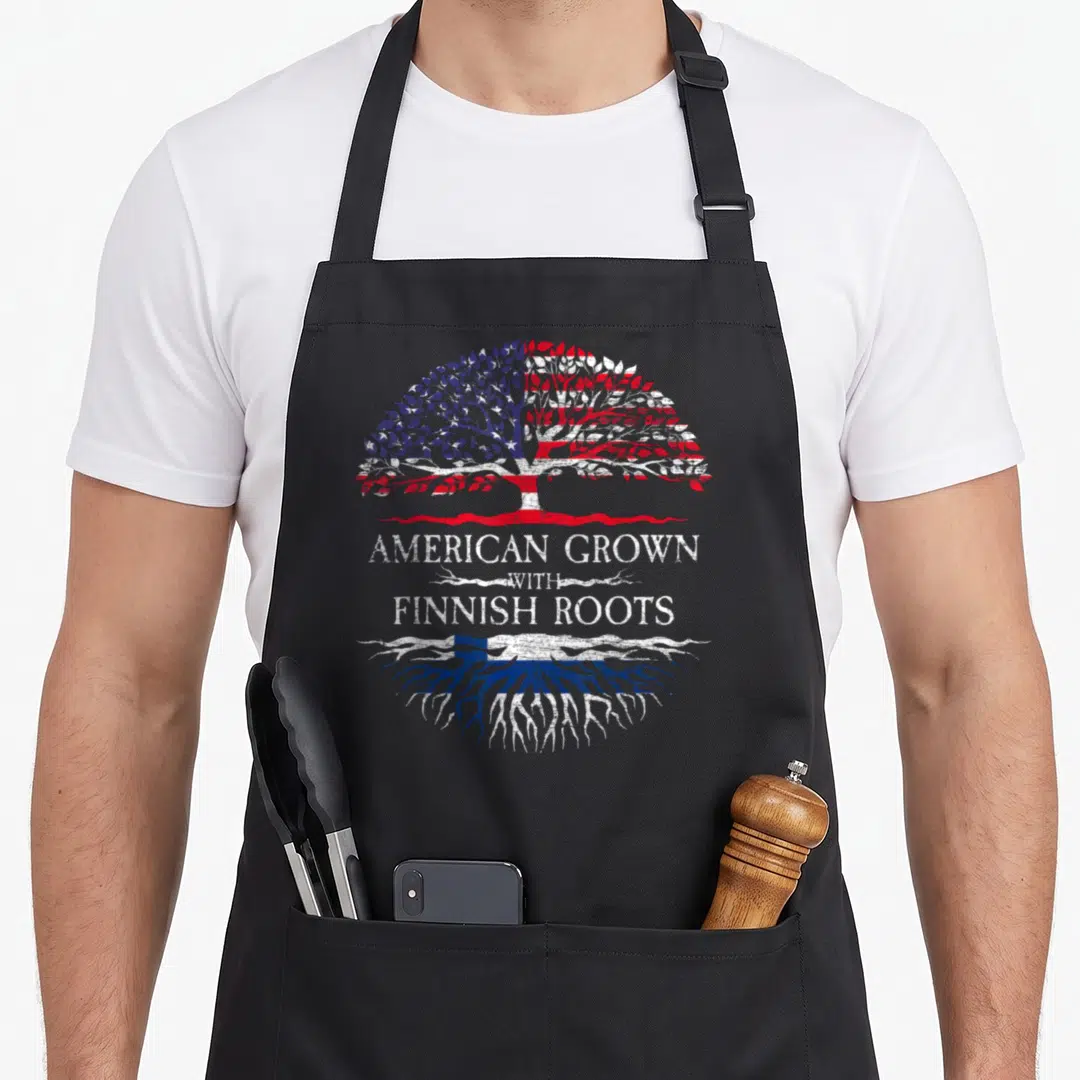Root finnish apron - Tree with US flag leaves and Finland flag roots split by text AMERICAN GROWN WITH FINNISH ROOTS — shown on a black cotton canvas apron against a white background