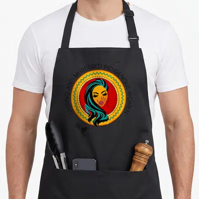 Missing native american apron - Cartoon woman face with red handprint inside yellow circle, arched text, small — shown on a black cotton canvas apron against a white background