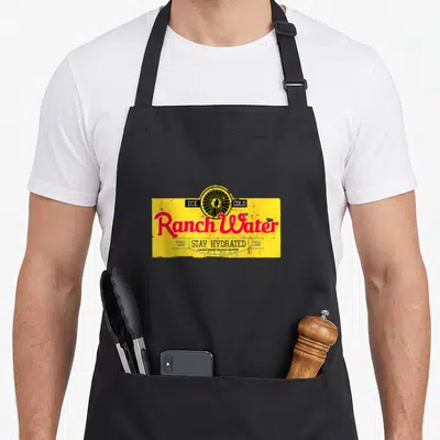 Drink southern aprons - Yellow rectangle with black wagon wheel, red Ranch Water script, and teal text listing tequila — shown on a black cotton canvas apron against a white background