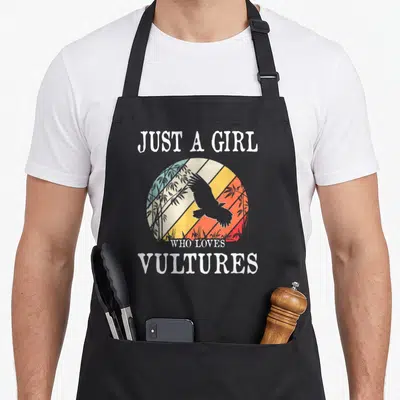 Funny vulture lover apron - Retro vulture silhouette inside a multi-colored sun circle with bamboo and white text — shown on a black cotton canvas apron against a white background