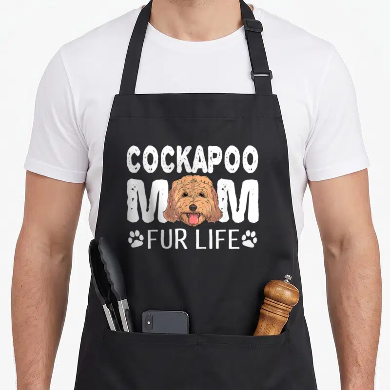 Fur cockapoo apron - Cartoon brown cockapoo head with COCKAPOO MOM FUR LIFE text and two paw prints — shown on a black cotton canvas apron against a white background