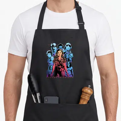 Populous novelty apron - Retro collage of Stranger Things characters with Eleven center, blue pink red text bottom — shown on a black cotton canvas apron against a white background