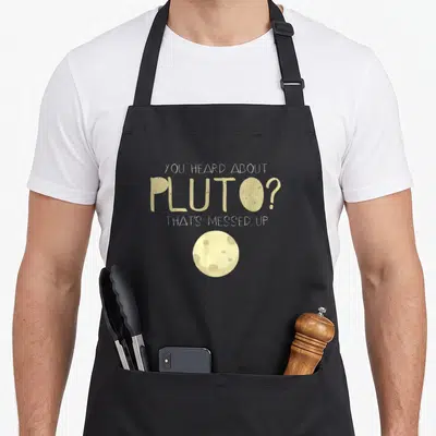 Pluto novelty apron - Beige text You Heard About Pluto That's Messed Up above small circular planet illustration — shown on a black cotton canvas apron against a white background