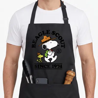 Woodstock beagle apron - Snoopy and Woodstock wearing hats with Beagle Scout text and 50 years since 1974 — shown on a black cotton canvas apron against a white background