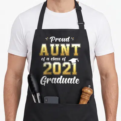 Aunt class funny apron - Proud Aunt of a class of 2021 Graduate text with small cap icon in white and gold — shown on a black cotton canvas apron against a white background
