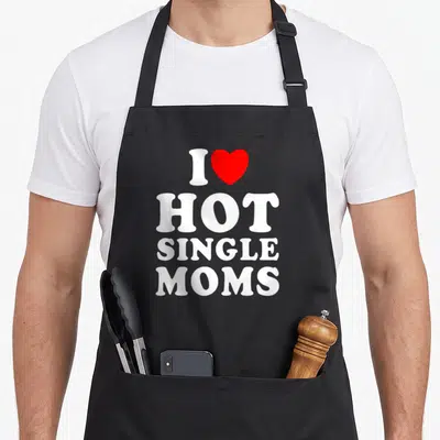 Single christmas apron - White text I HOT SINGLE MOMS with a red heart symbol on grey background — shown on a black cotton canvas apron against a white background