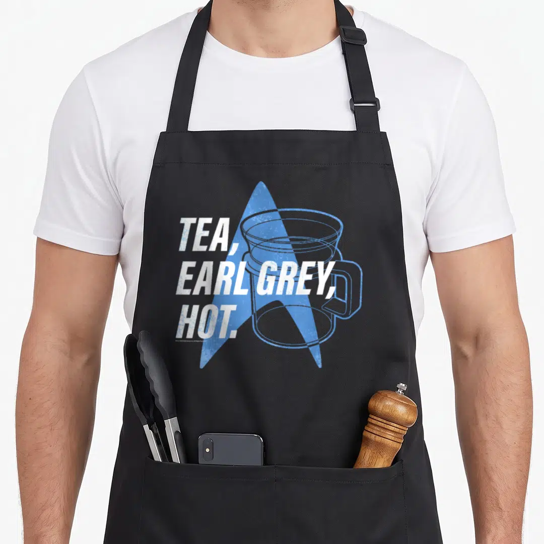Generation tea apron - Stacked TEA EARL GREY HOT text over blue star and cup outline — shown on a black cotton canvas apron against a white background