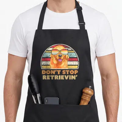 Retrieving golden retriever apron - Golden retriever head with retro sunglasses and striped background under text Don't — shown on a black cotton canvas apron against a white background
