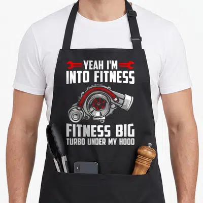 Fitness car apron - Grey turbocharger with red accents and white text flanked by two red wrenches — shown on a black cotton canvas apron against a white background