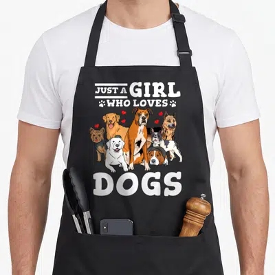 Boxer dog apron for women - Six cartoon dogs in white brown tan and red below Just a Girl Who Loves Dogs text with red — shown on a black cotton canvas apron against a white background