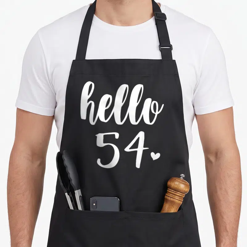 Fifty four birthday apron - Stacked white hello 54 typography with small heart on grey background — shown on a black cotton canvas apron against a white background
