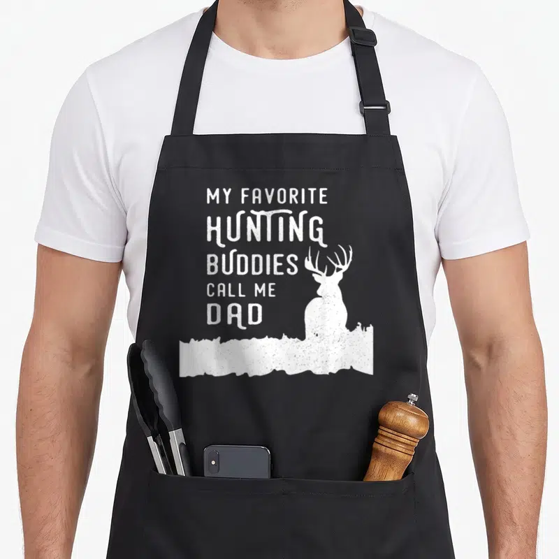 Hunter dad and son aprons - White distressed text My Favorite Hunting Buddies Call Me Dad with deer silhouette in grass — shown on a black cotton canvas apron against a white background