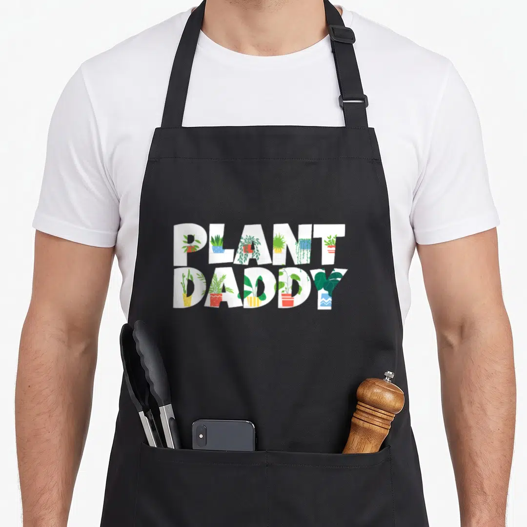Plant daddy apron - PLANT DADDY text with potted plants inside letters in white green red blue yellow — shown on a black cotton canvas apron against a white background
