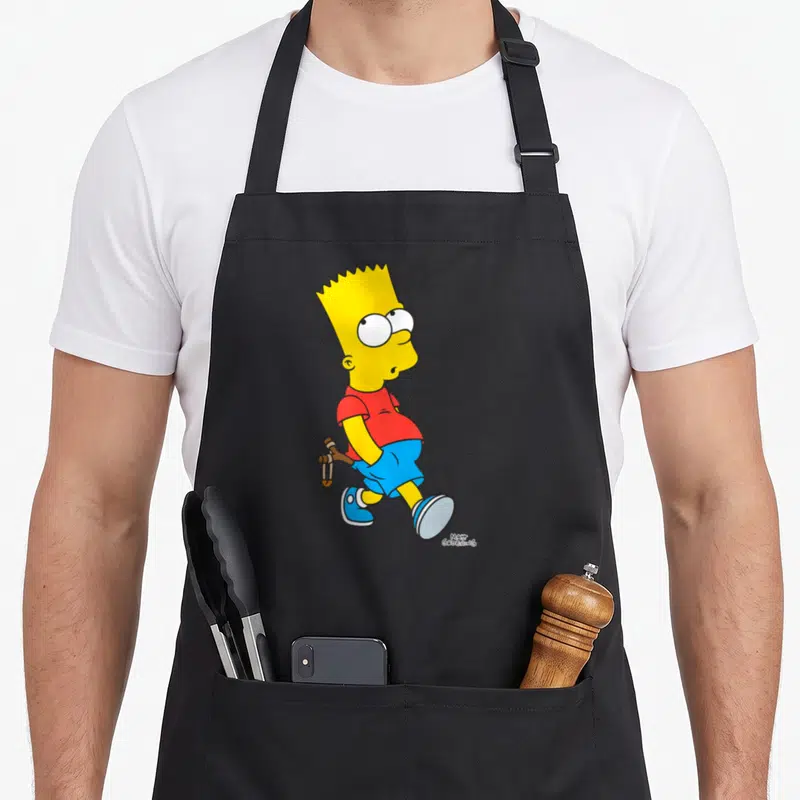 Slingshot simpson apron - Bart Simpson standing with a slingshot in yellow red and blue cartoon art — shown on a black cotton canvas apron against a white background