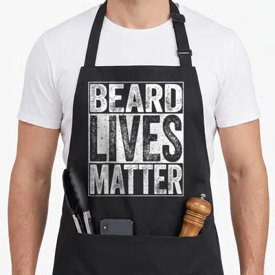 Live beard apron - White distressed text reading BEARD LIVES MATTER stacked vertically inside a rectangular border — shown on a black cotton canvas apron against a white background