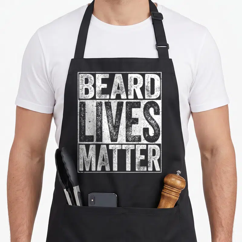 Live beard apron - White distressed text reading BEARD LIVES MATTER stacked vertically inside a rectangular border — shown on a black cotton canvas apron against a white background