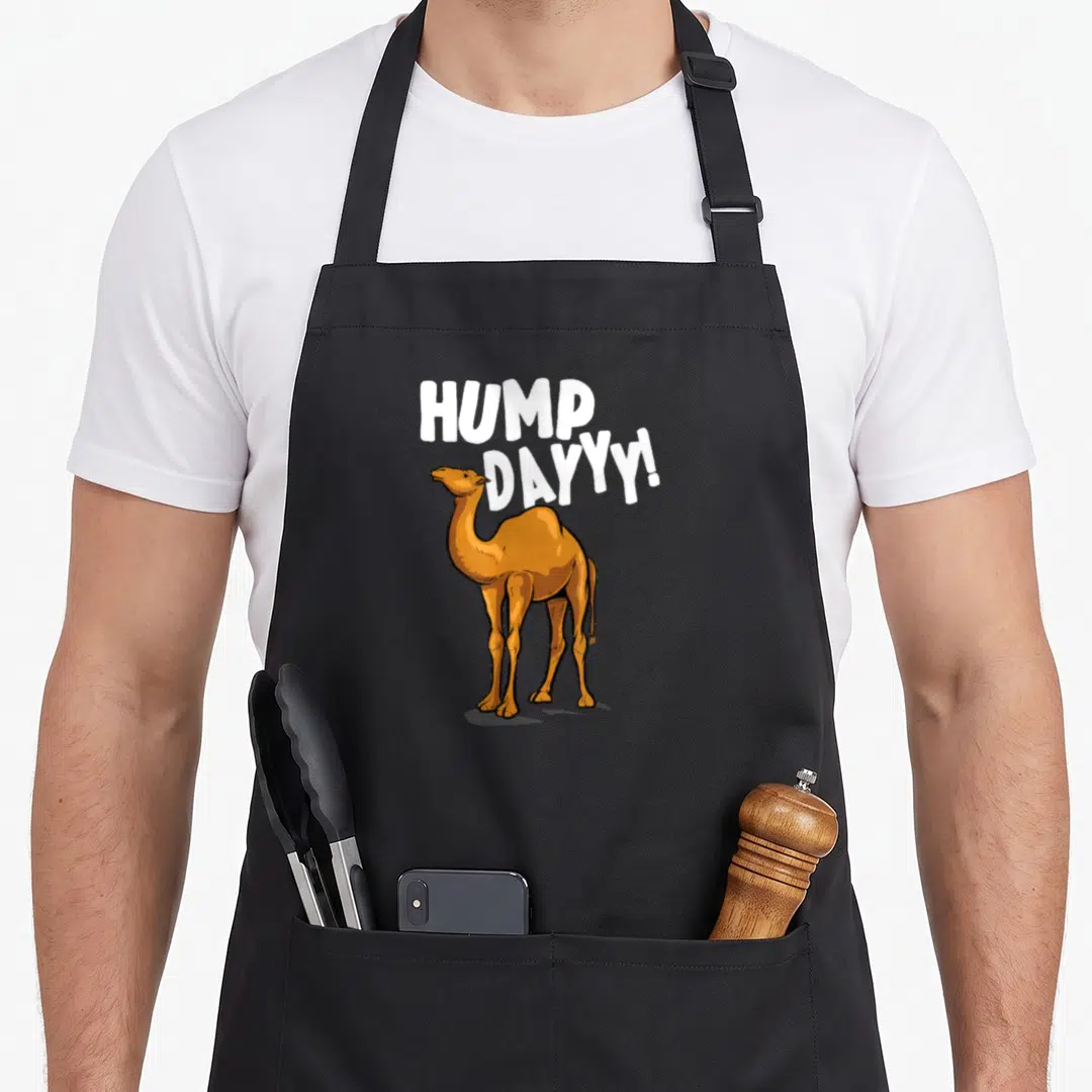 Camel dromedary apron - Brown cartoon camel standing under white HUMP DAYYY! text — shown on a black cotton canvas apron against a white background