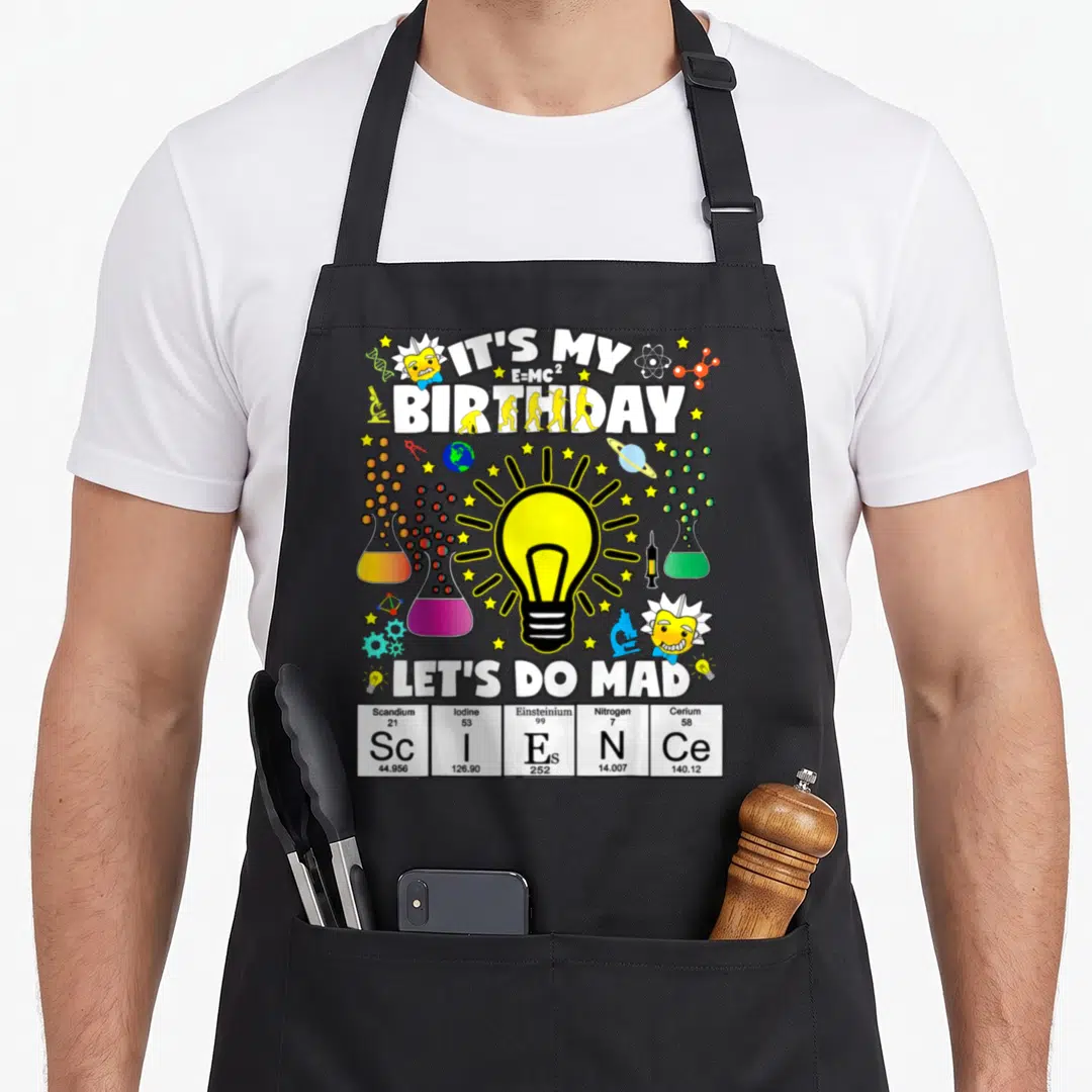 Theme science apron - Light bulb surrounded by flasks, Einstein heads, and periodic table cells spelling ScIENCe — shown on a black cotton canvas apron against a white background