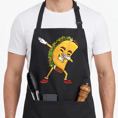 Dab mexican apron - Cartoon taco with arms legs face white gloves red shoes dabbing pose — shown on a black cotton canvas apron against a white background