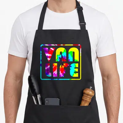 Van promo aprons - Stacked VAN LIFE text in purple blue yellow red and green tie-dye inside a rounded border — shown on a black cotton canvas apron against a white background