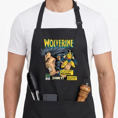 Logan hobby apron - Wolverine comic profile head action pose yellow blue black text boxes SNKT — shown on a black cotton canvas apron against a white background
